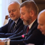 Trzy osoby w garniturach siedzą przy stole konferencyjnym podczas formalnego spotkania